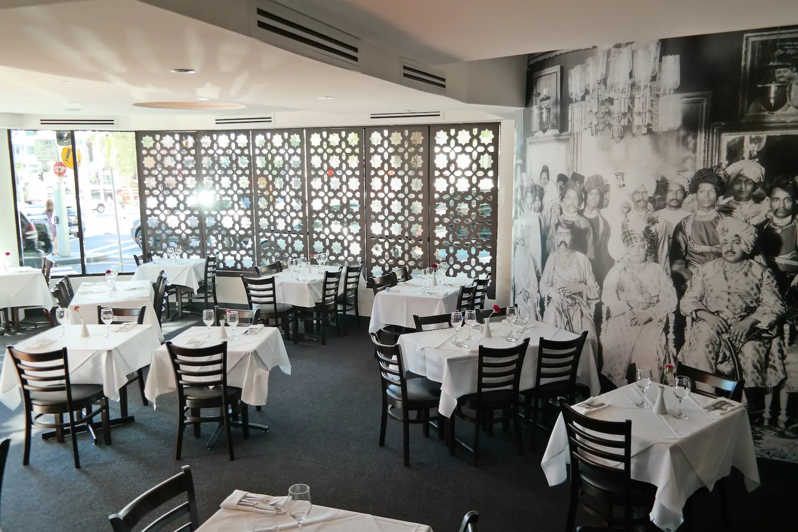 The Malabar dining room in daylight: white-clothed tables, dark timber chairs, a carved screen along the windows and a large black-and-white mural on the right-hand wall.
