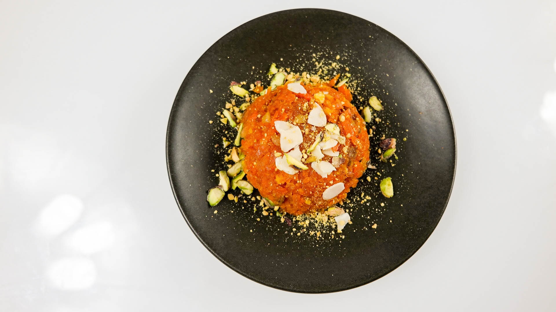 Carrot halwa topped with flaked coconut and pistachio on a dark plate