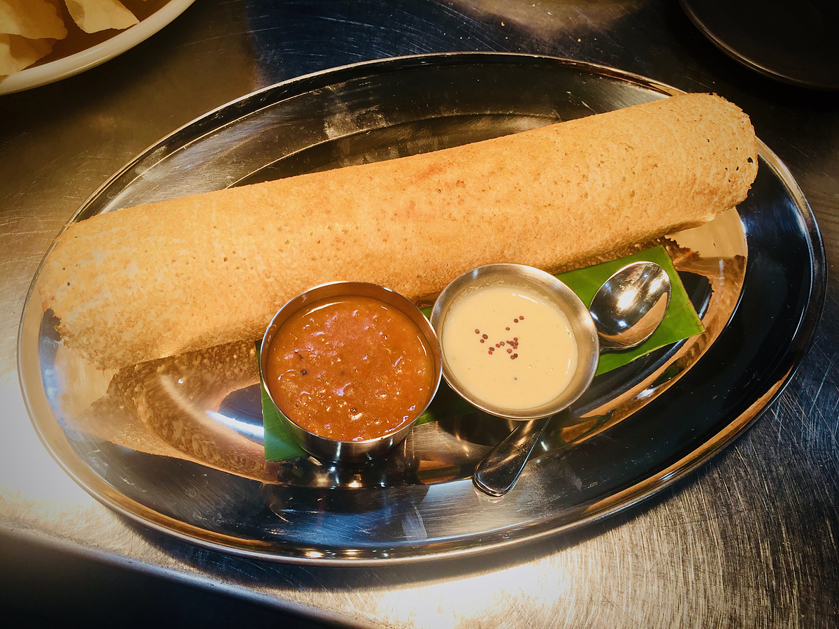 A crisp dosai on a steel platter with sambar and coconut chutney
